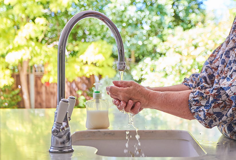 An older woman running her hands underneath cold water from a kitchen tap
