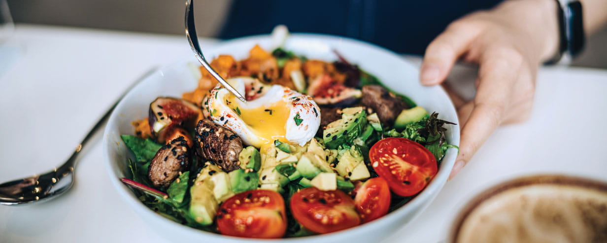 Close up of a dish with a soft boiled egg on top of a salad
