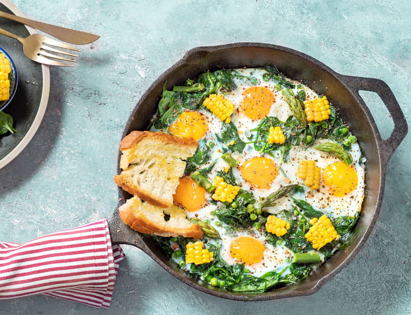 Shakshuka eggs spinach in a cast iron pan with a red and white tea towel wrapped around the handle