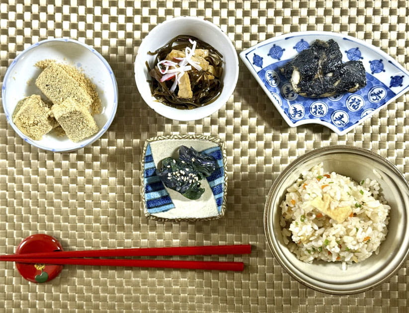 A typical Okinawan meal in several small dishes on a woven mat with a pair of red chopsticks