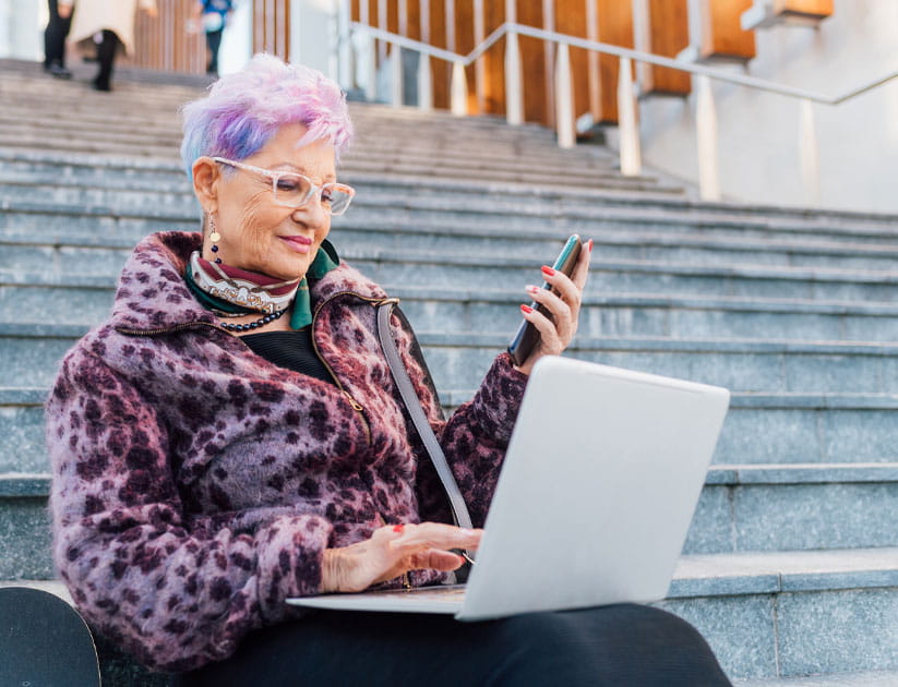 Italy, Fashionable senior woman using laptop on steps in city
