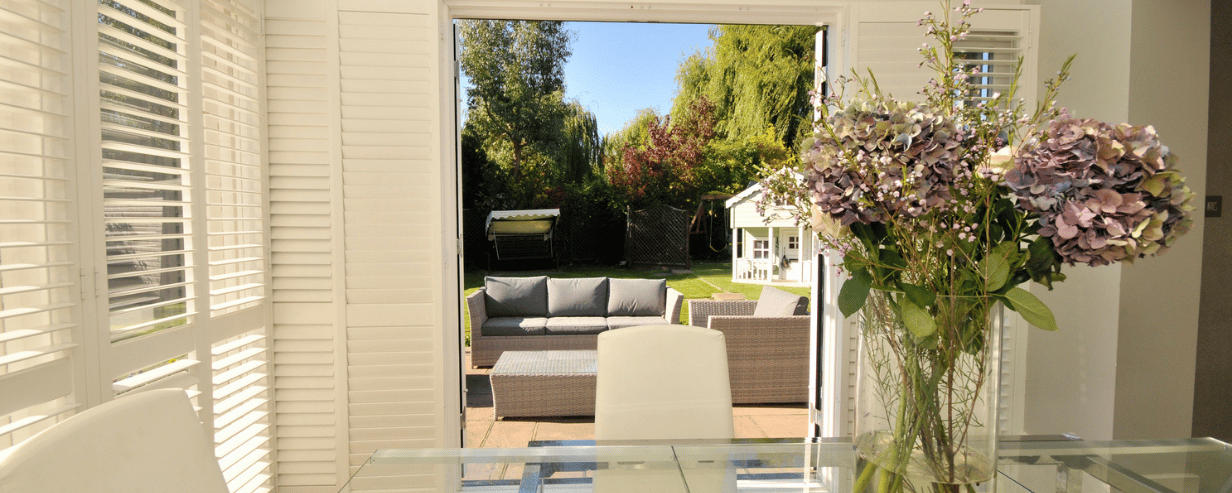 A cool conservatory with blinds looking out into a sun drenched garden