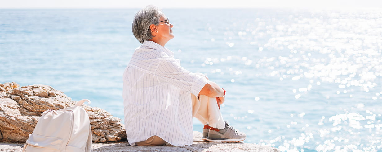 Beautiful middle aged woman with grey hair in casual clothes sitting and looking on view of sea