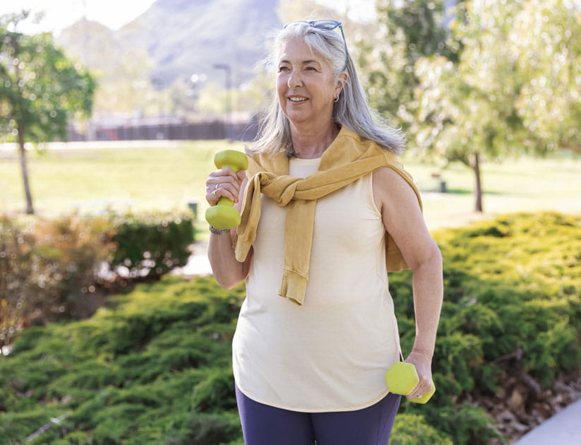 Athletic senior woman walking with hand weights in the park