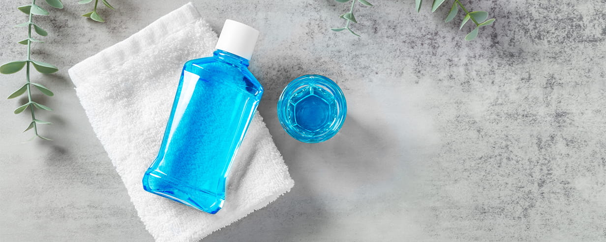 Mouthwash on white towel with cup and eucalyptus on grey table