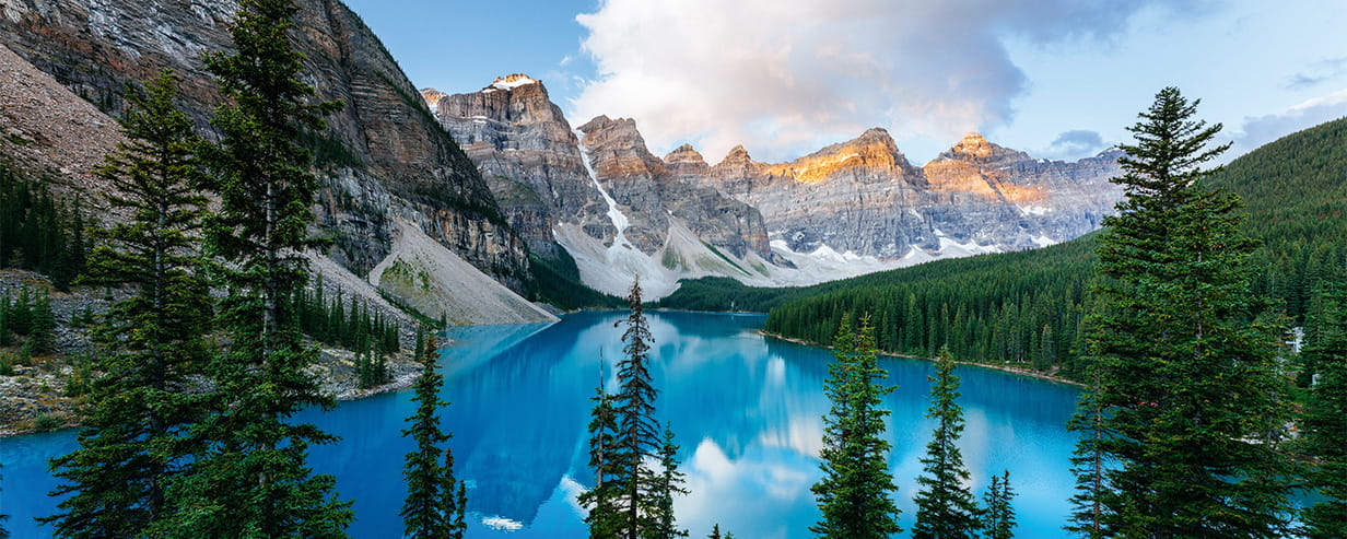 A blue lake with trees and the Rocky mountains in the background