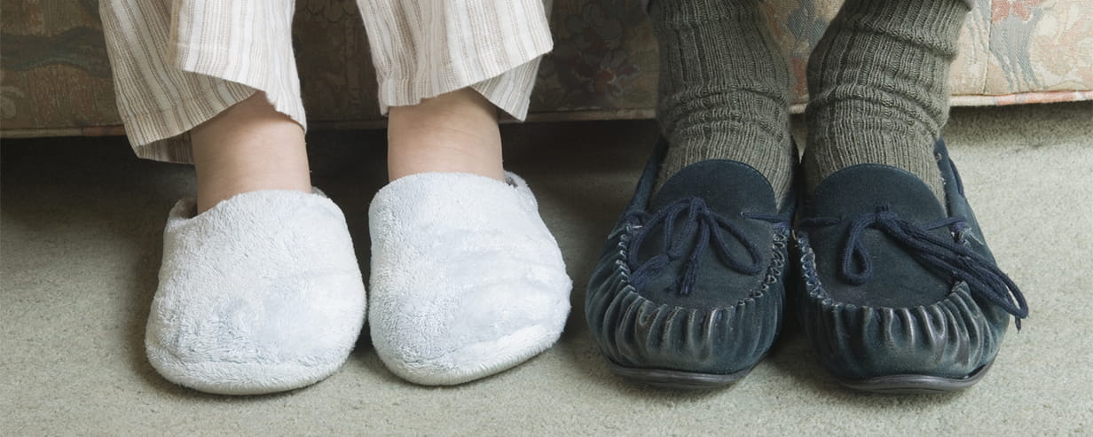 Two home slippers worn by people sitting on the couch