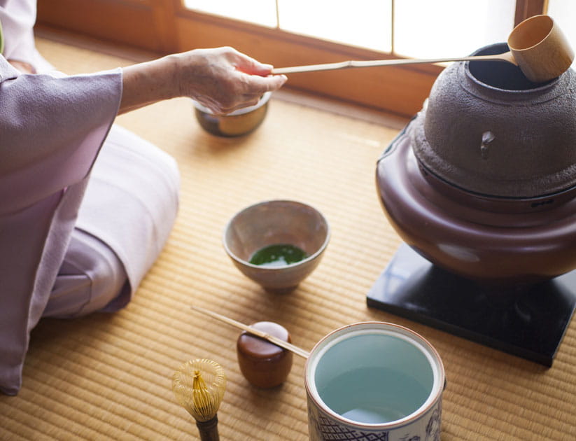 Mature person in a kimono preparing a matcha tea for a traditional Japanese tea party
