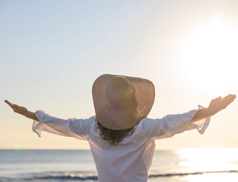 Mature woman with her arms outstretched wearing a straw hat at the beach for sunrise