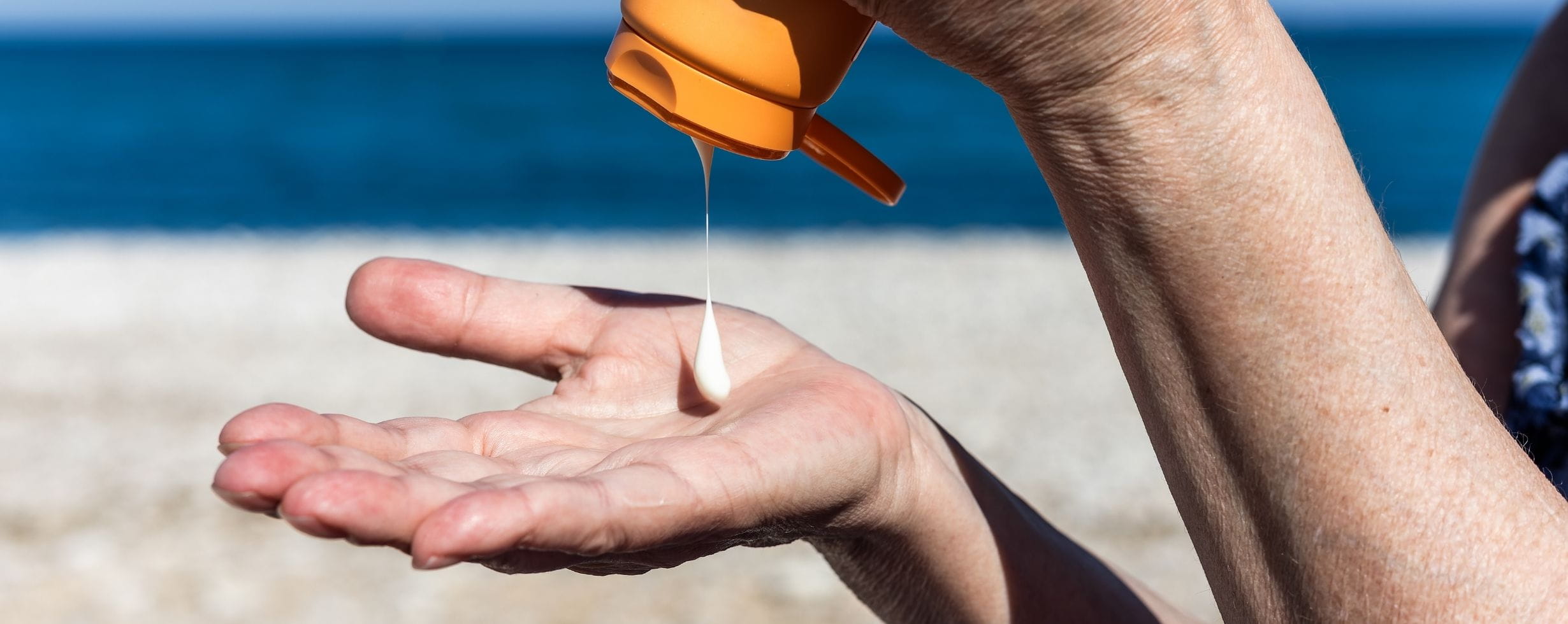 A woman squeezing out sunscreen onto the palm of her hand while at the beach