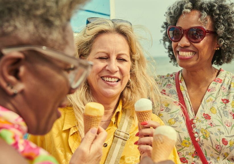 Three mature aged women eat ice cream cones together,smiling and wearing sunglasses