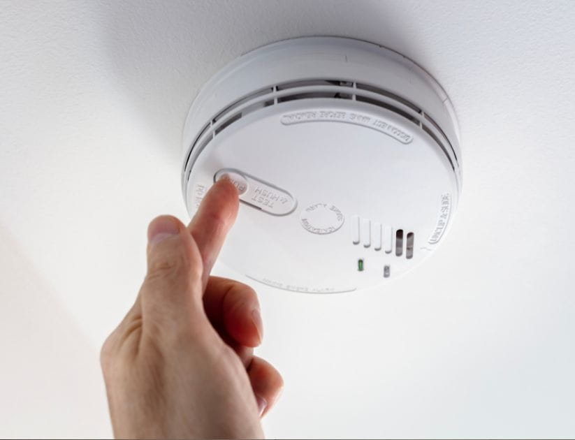 A close up of a smoke alarm with someone pressing the reset button