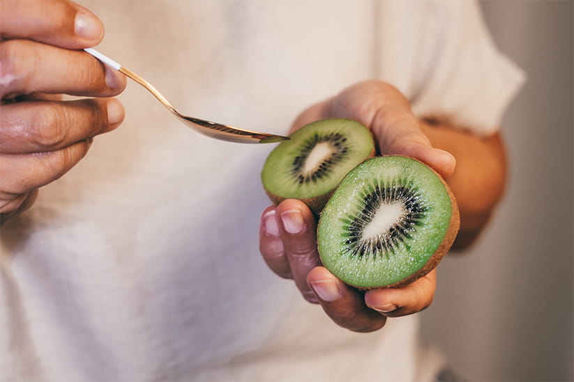 Woman's hand holding a ripe green kiwi fruit cut in half ready to eat.