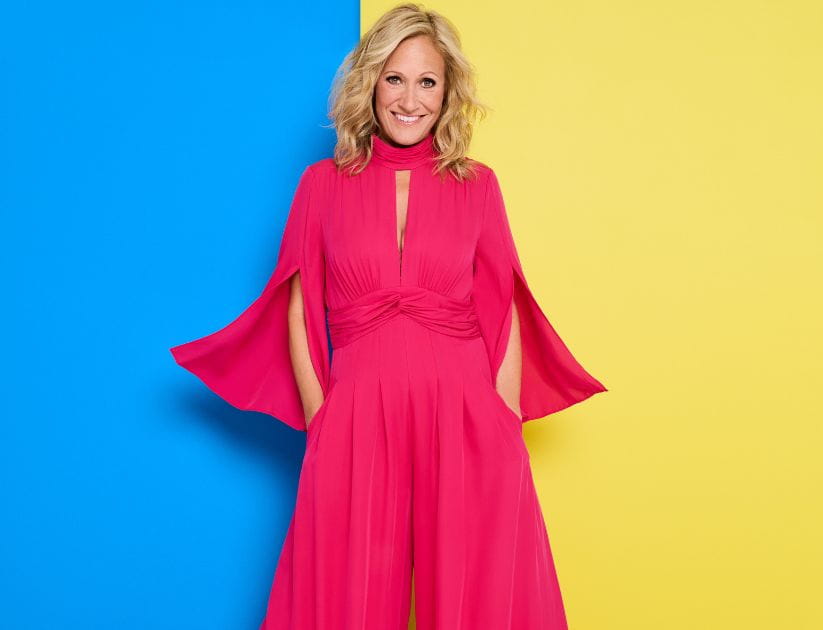 A portrait of Sophie Raworth in a pink dress with a yellow and blue background