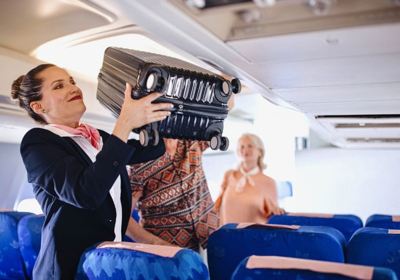 An air hostess puts cabin luggage in an overhead locker on the plane