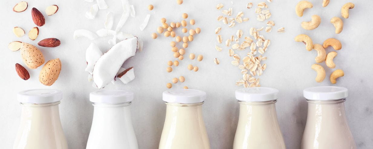 A variety of non dairy milk viewed from above over a white marble background