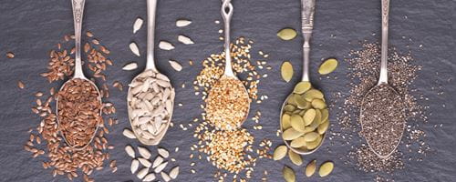 5 spoons each heaped with different seed types including pumpkin, sunflower and chia seeds