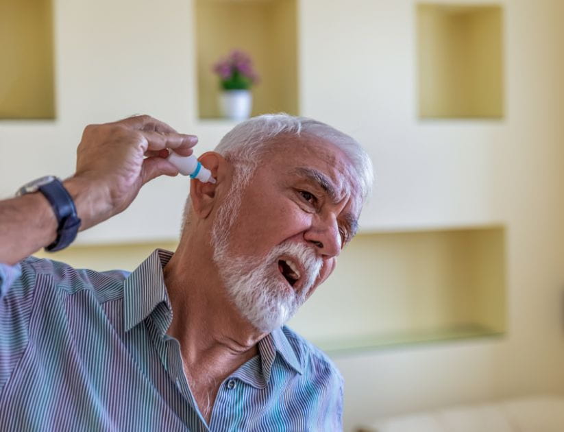 A man using a bottle of eardrops due to hearing problems