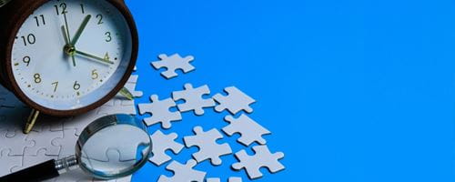 Jigsaw puzzle with an alarm clock and magnifying glass next to it