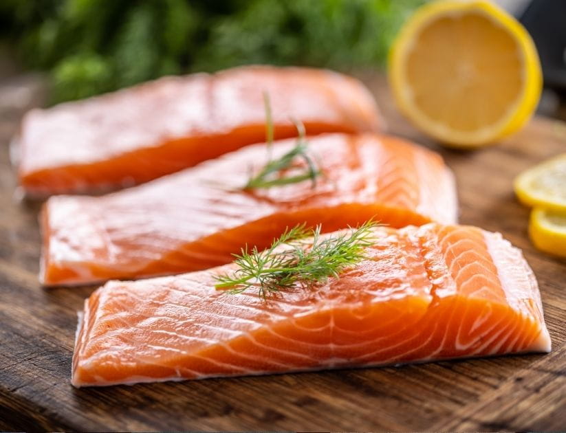 salmon fillets on a wooden cutting board with dill, rosemary and lemon on trop