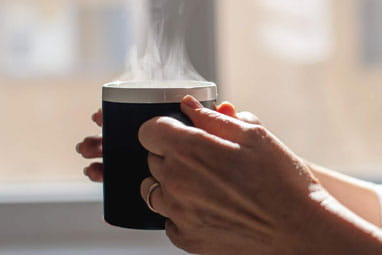 Mature hands holding a mug with steam coming off the top