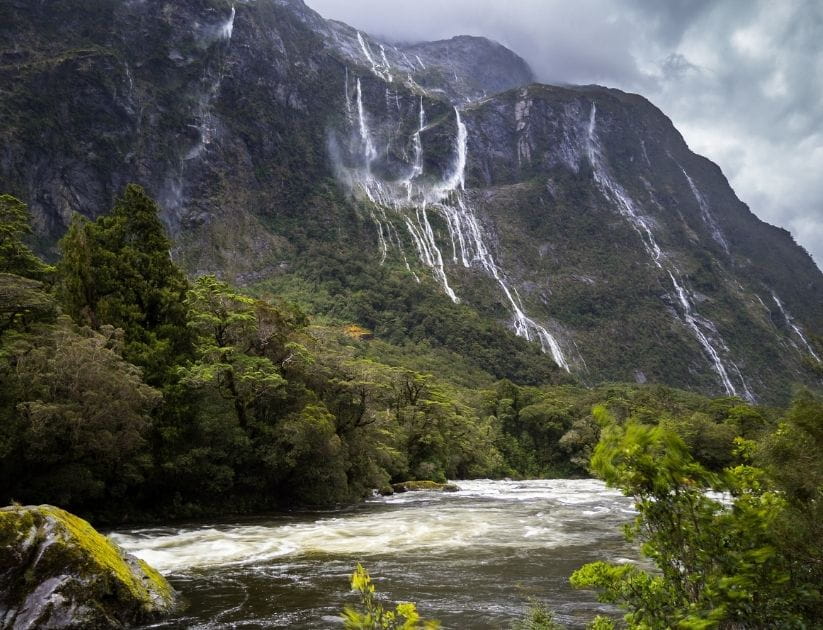 A landscape view of mountains and waterfalls on a cloudy day in Cleddau Valley in Fjordland National Park, New Zealand