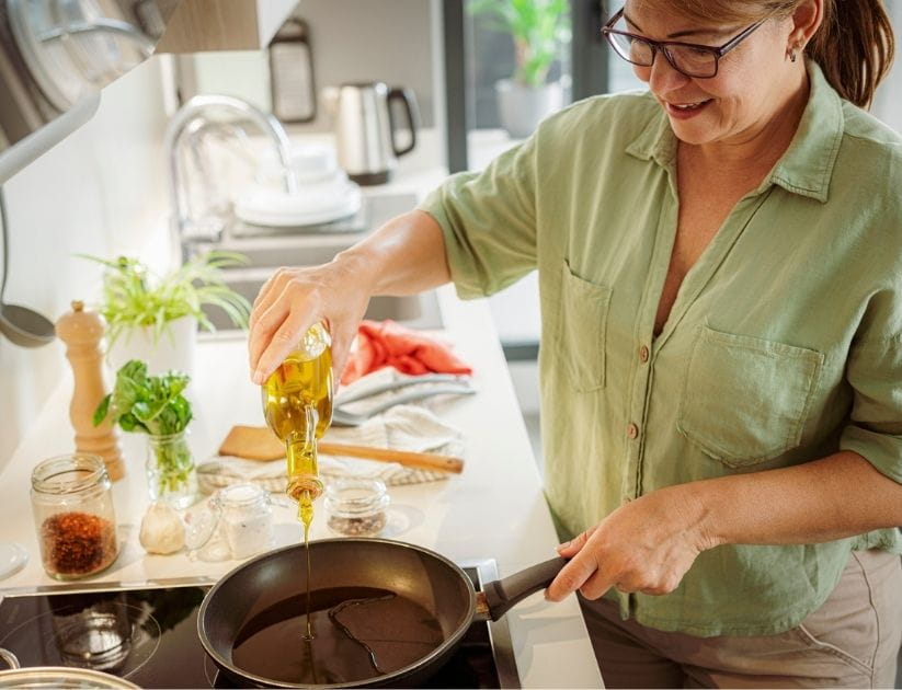 Smiling woman adding cooking oil to a frying pan