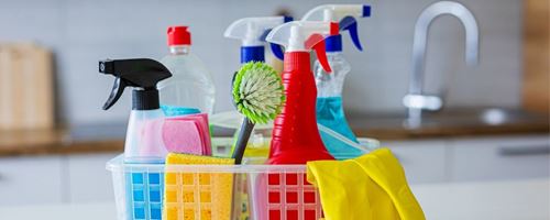 A plastic basket filled with various cleaning supplies placed on a white kitchen countertop