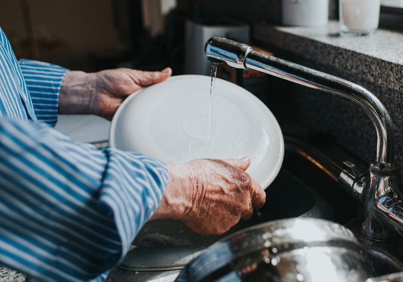 A man rinses a plate under a tap