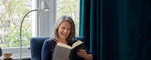 Mature smiling woman reading a book with a serious readers light illuminating the pages