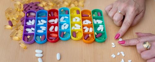 A lady splits a white pill in half with her fingers to organize them for medication