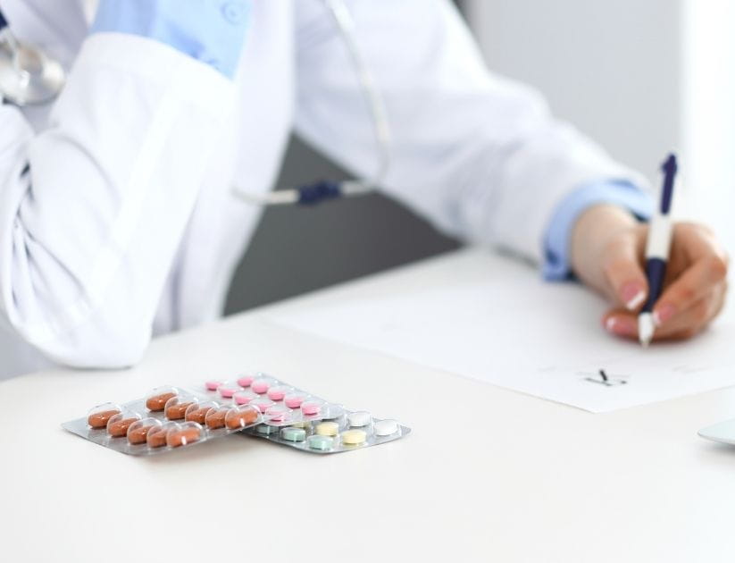 A doctor filling up prescription form while sitting at the desk in hospital