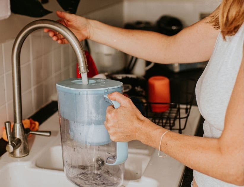 Woman filling a water filter jug at the kitchen sink