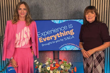 Trinny Woodall and Lorraine standing by a screen with the Experience is Everything logo