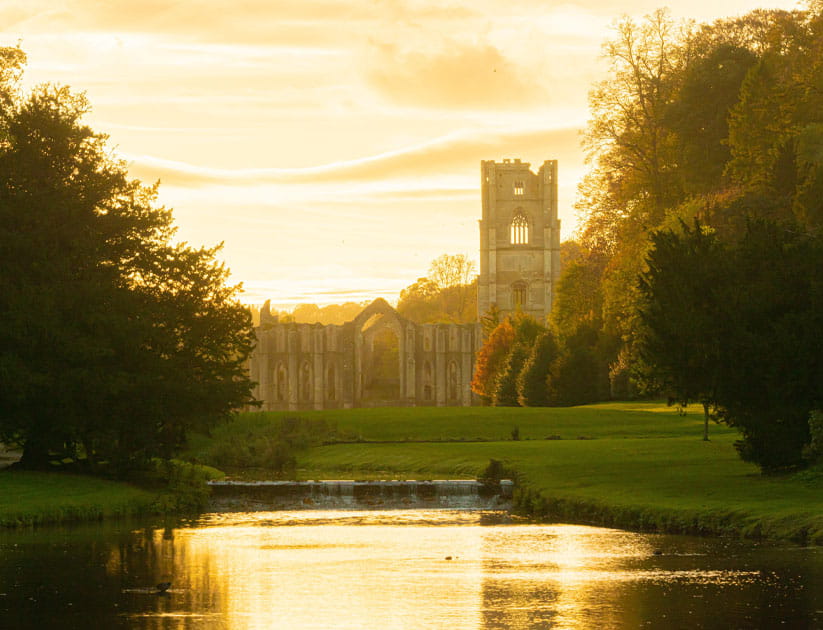 The ruins of Fountains Abbey with the sunlight shining from behind them