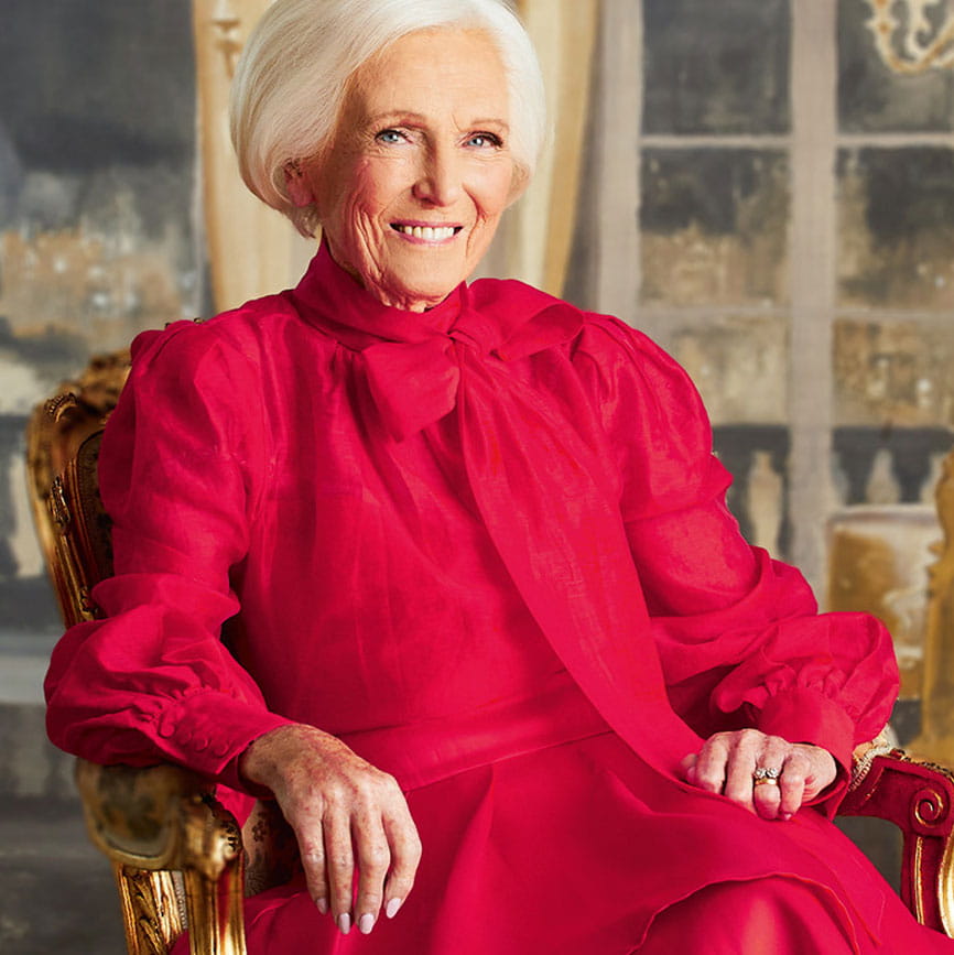 Mary berry in a red dress sitting in a golden chair