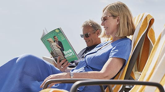 Two people on the sun deck of Saga's Spirit of Adventure reading a Saga magazine
