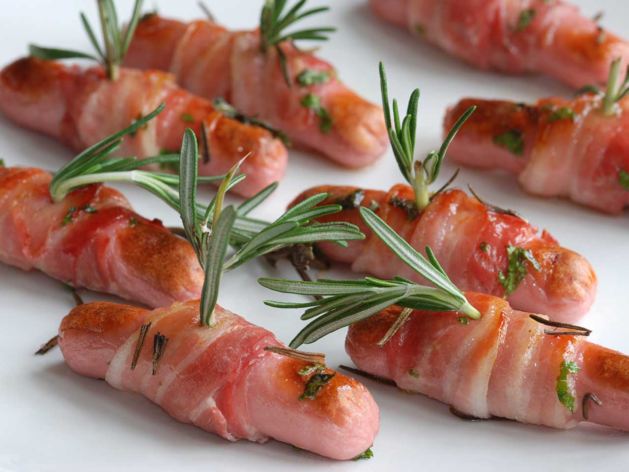 Sausages wrapped in bacon with a sprig of rosemary garnishing each