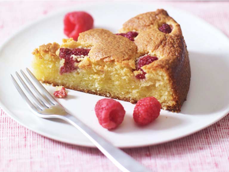 A slice of cake on a plate, with raspberries and a fork