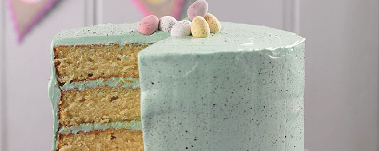 A 3 layer cake with speckled blue icing topped with mini Easter eggs