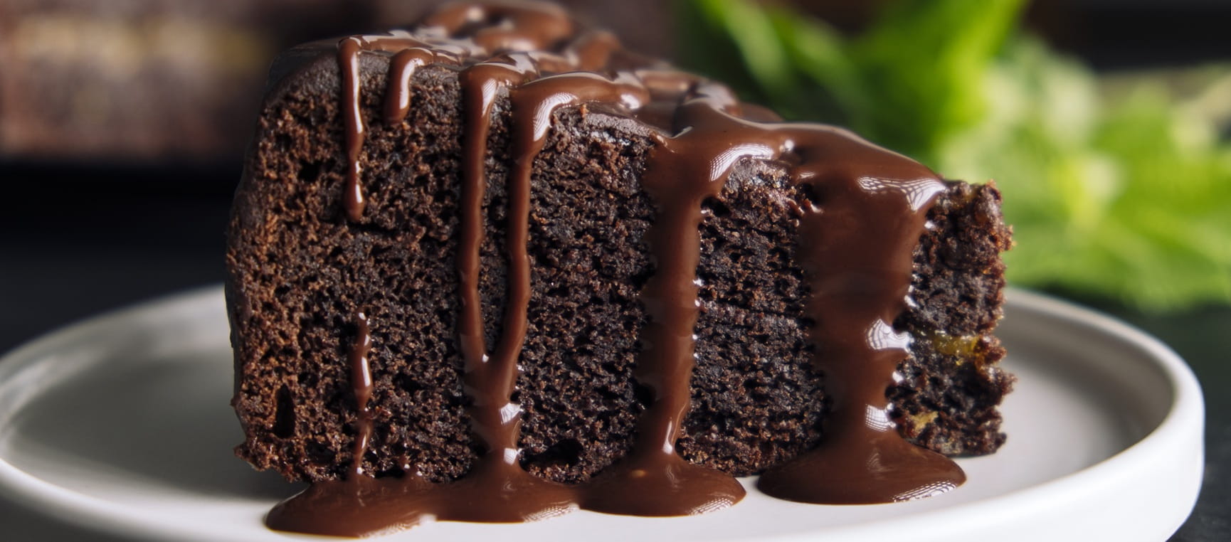 A slice of chocolate cake on a white plate with chocolate icing running down the sides