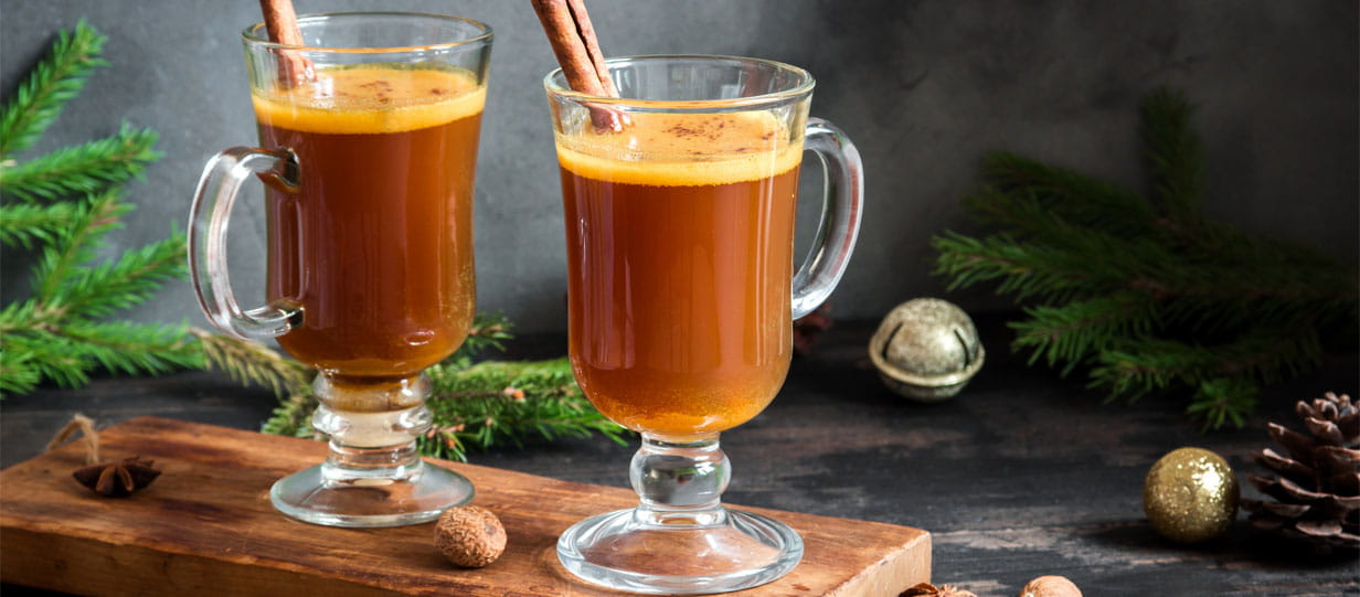 Glass mugs of hot buttered rum with sticks of cinnamon