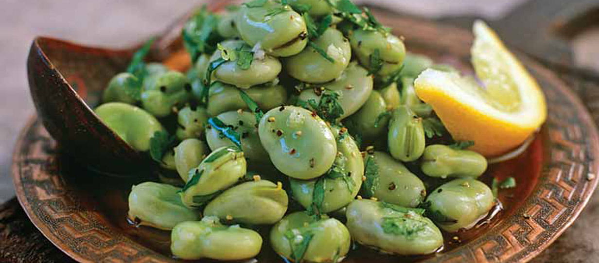 A foul moukala - fresh broad bean salad on a copper dish with a slice of lemon and a serving spoon