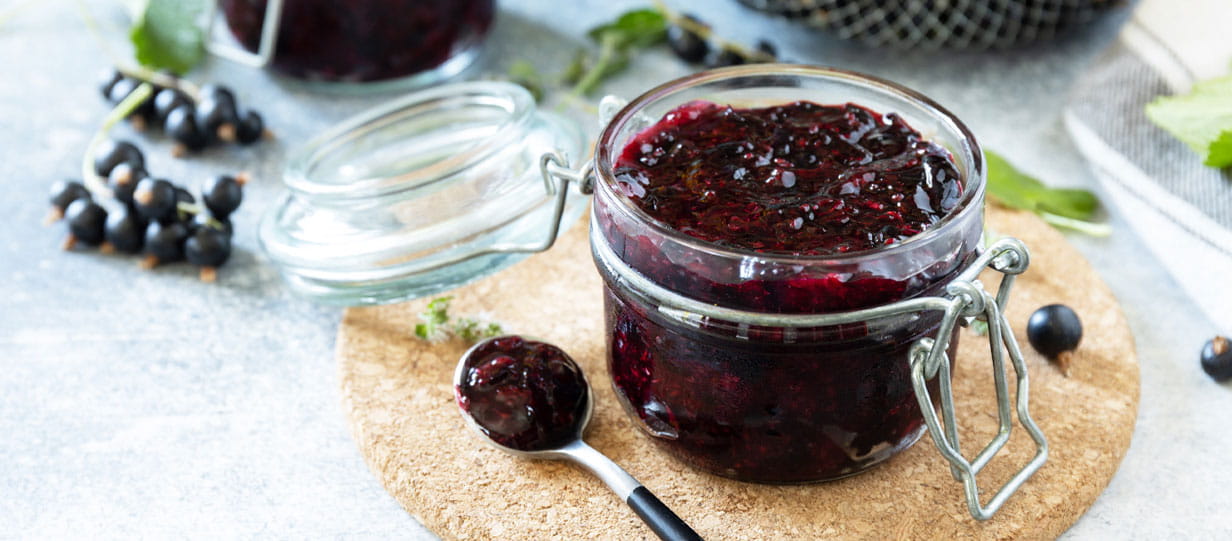 Blackcurrant jam in an open mason jar with a spoon on the table next to it