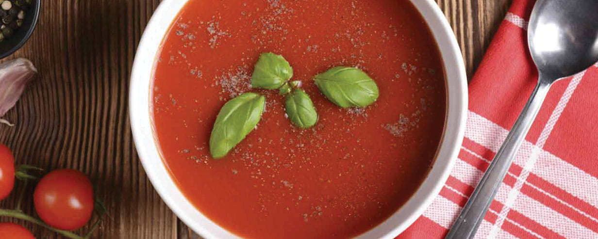 Tomato soup garnished with basil leaves in white bowl