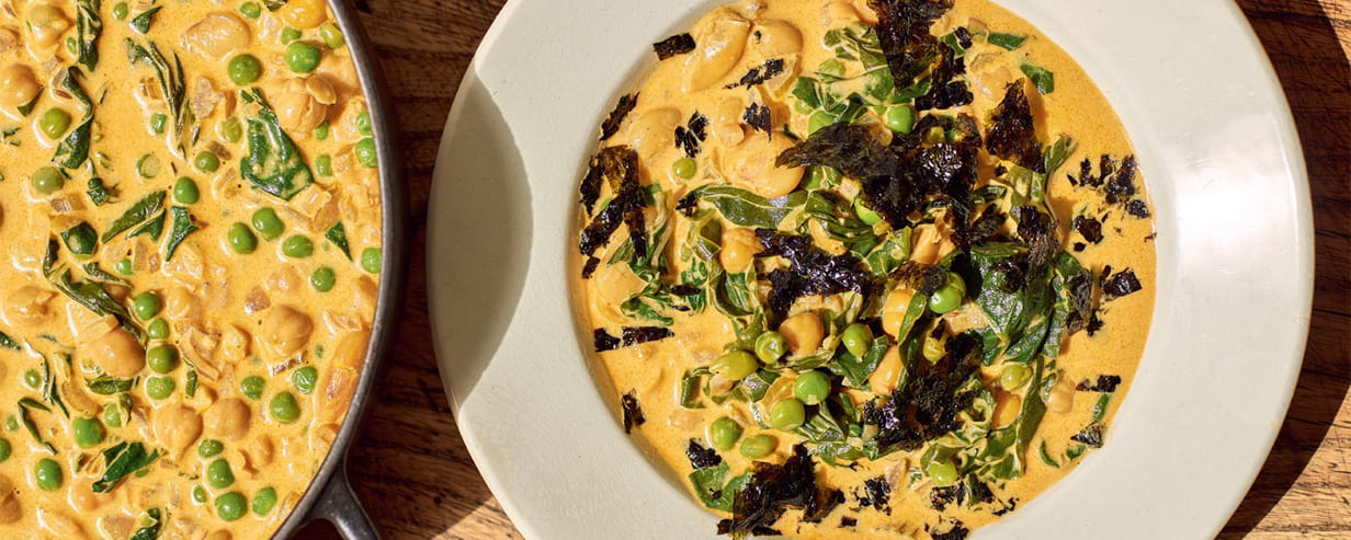 A curried bean and coconut stoup in a bowl and a stockpot on a rustic wooden table