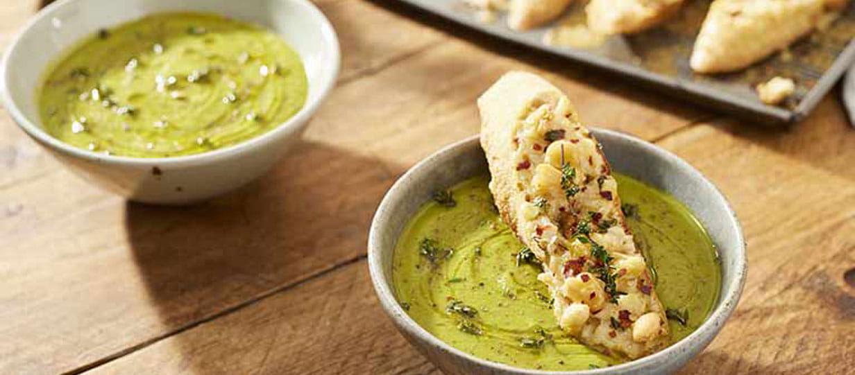 Bowls of soups, one topped with a large crouton. More croutons on a baking try in the background.