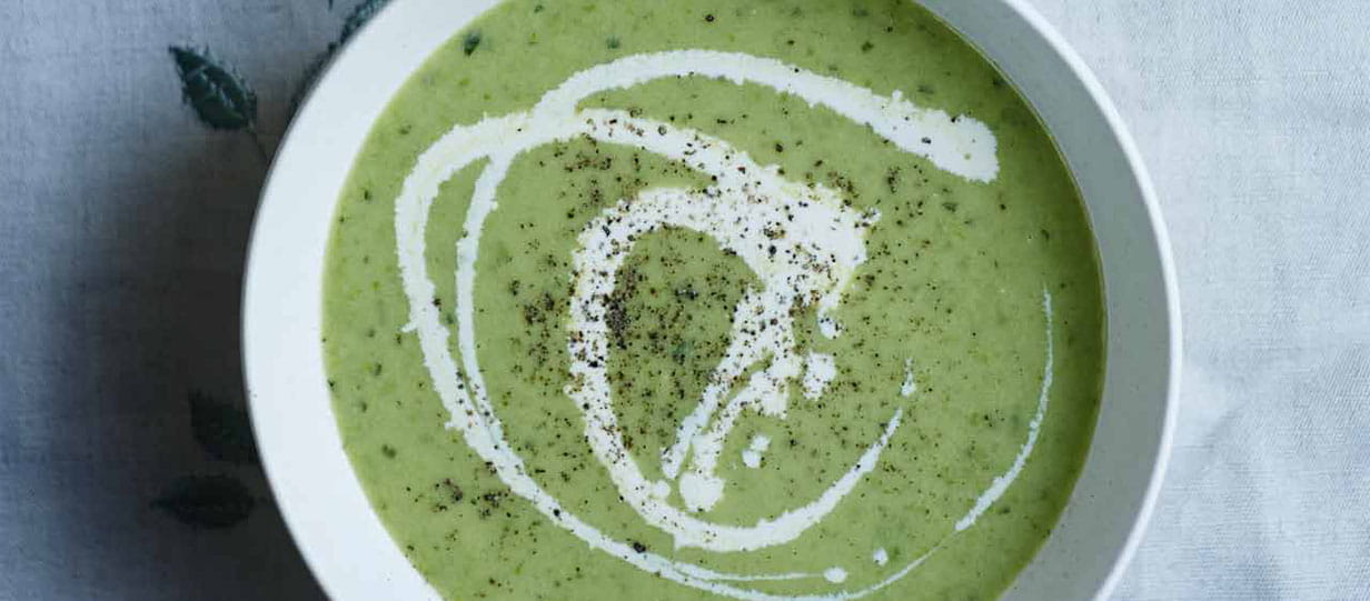 Bowl of pea soup topped with swirls of cream