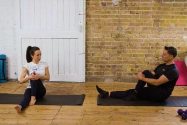 A man and woman sat on the floor stretching their legs