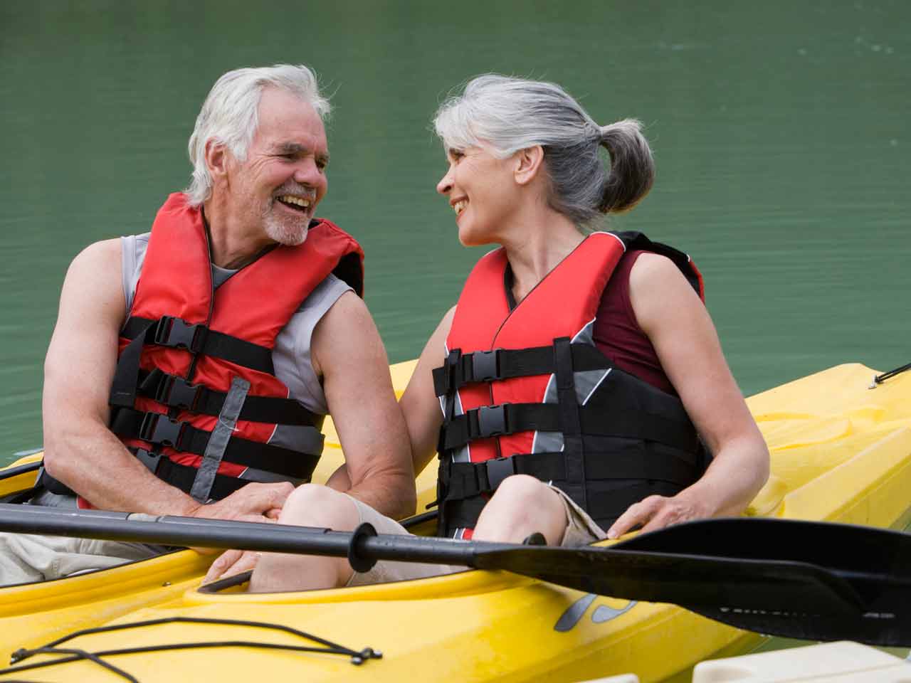 A mature couple wearing red life vests kayaking in two separate yellow kayaks